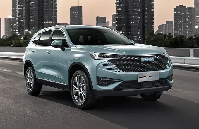 A light blue Haval H6 HEV SUV parked on a city street at dusk, with modern buildings in the background and streetlights illuminating the scene.